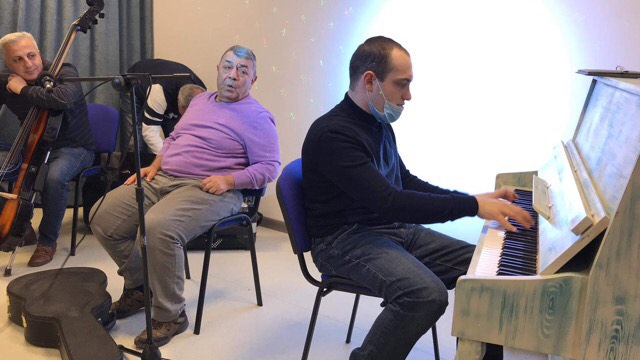 Ruben Hakhverdayan and a band member listen  as young Raphael plays on the piano.